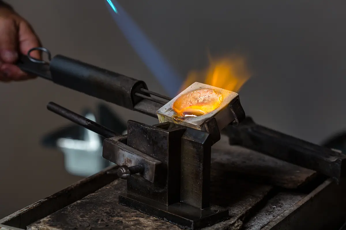 Molten gold glowing in a small crucible under a torch flame