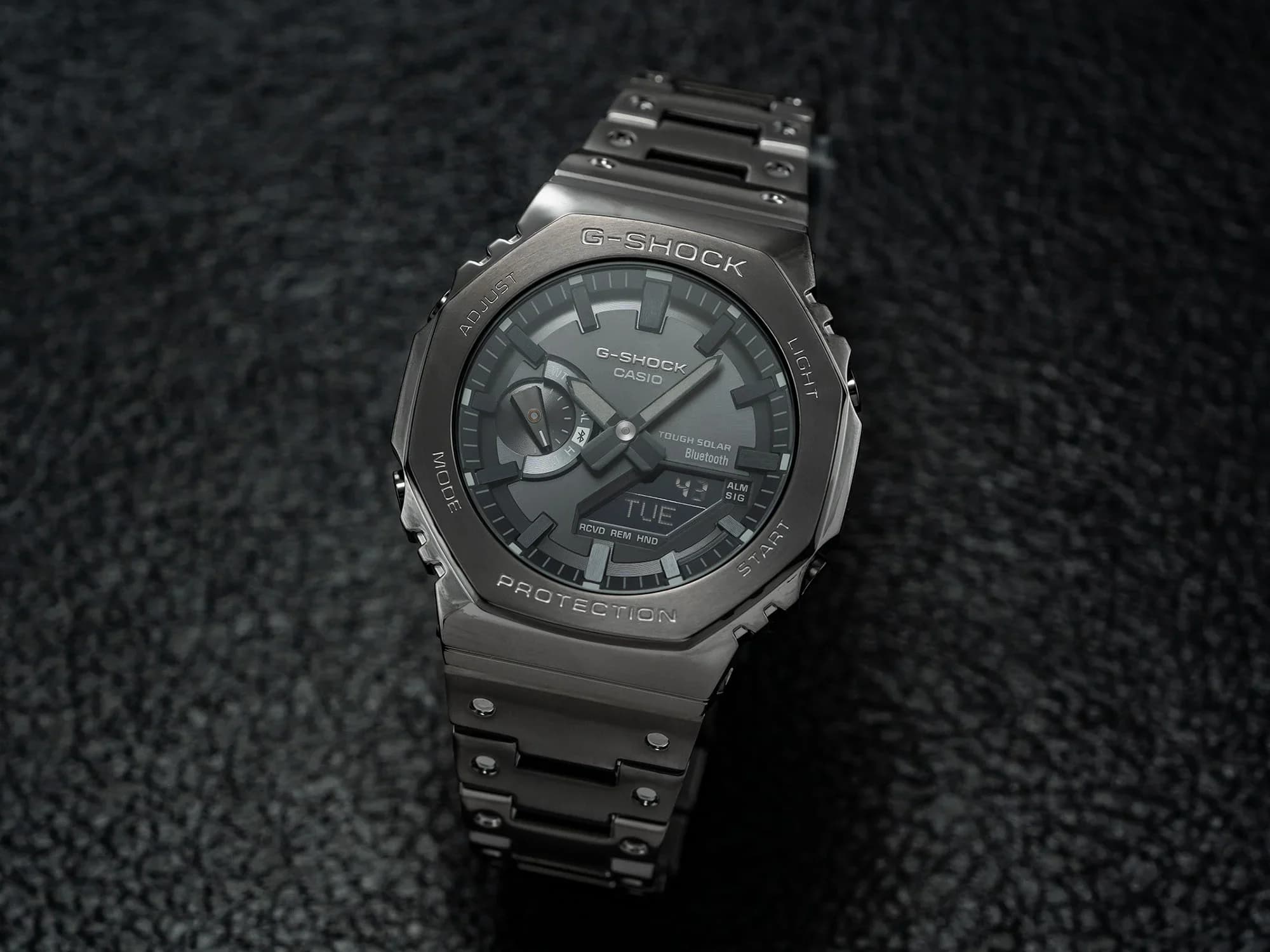 Black full-metal G-Shock 2100 with an octagonal bezel, on a dark textured surface