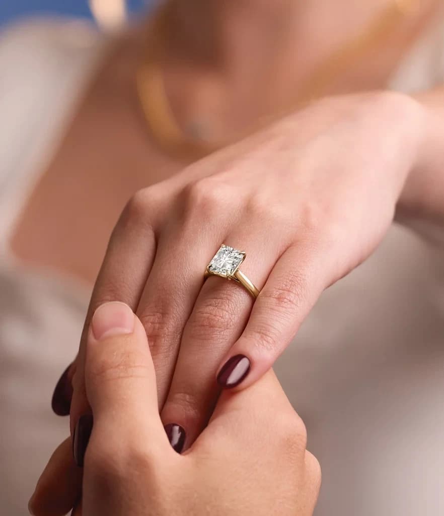 Diamond solitaire engagement ring in yellow gold, worn on a hand held in another