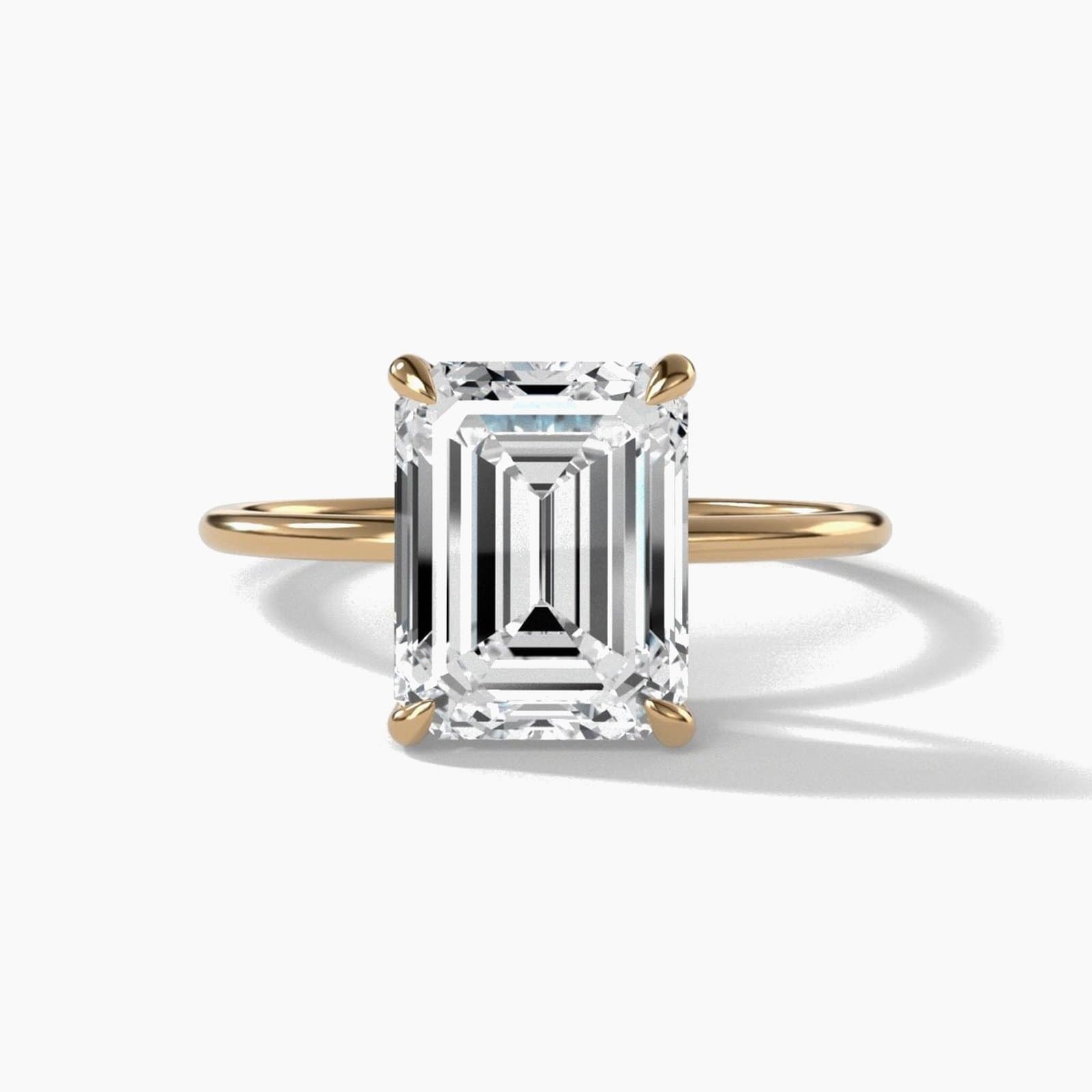 Thin solitaire engagement ring with an emerald-cut diamond in yellow gold